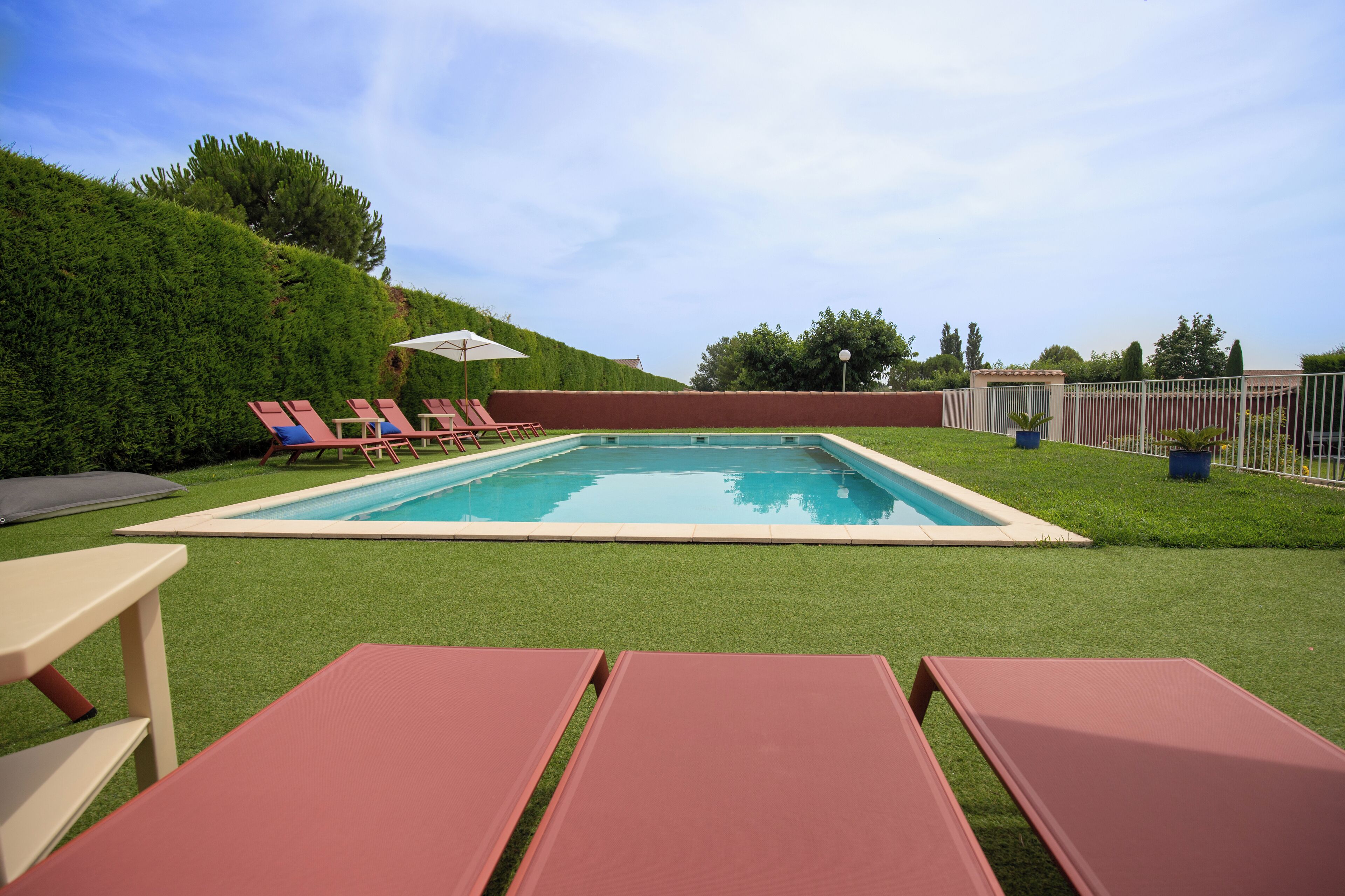 Une piscine rectangulaire entourée d’une pelouse, avec quelques chaises longues et une table.