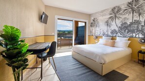 Ett hotellrum med en säng, ett skrivbord, en stol, en TV, en balkong med utsikt och en väggmålning.