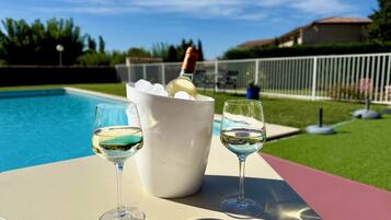 Escena junto a la piscina con un cubo blanco que contiene una botella y hielo, y dos copas de vino blanco sobre una mesa.