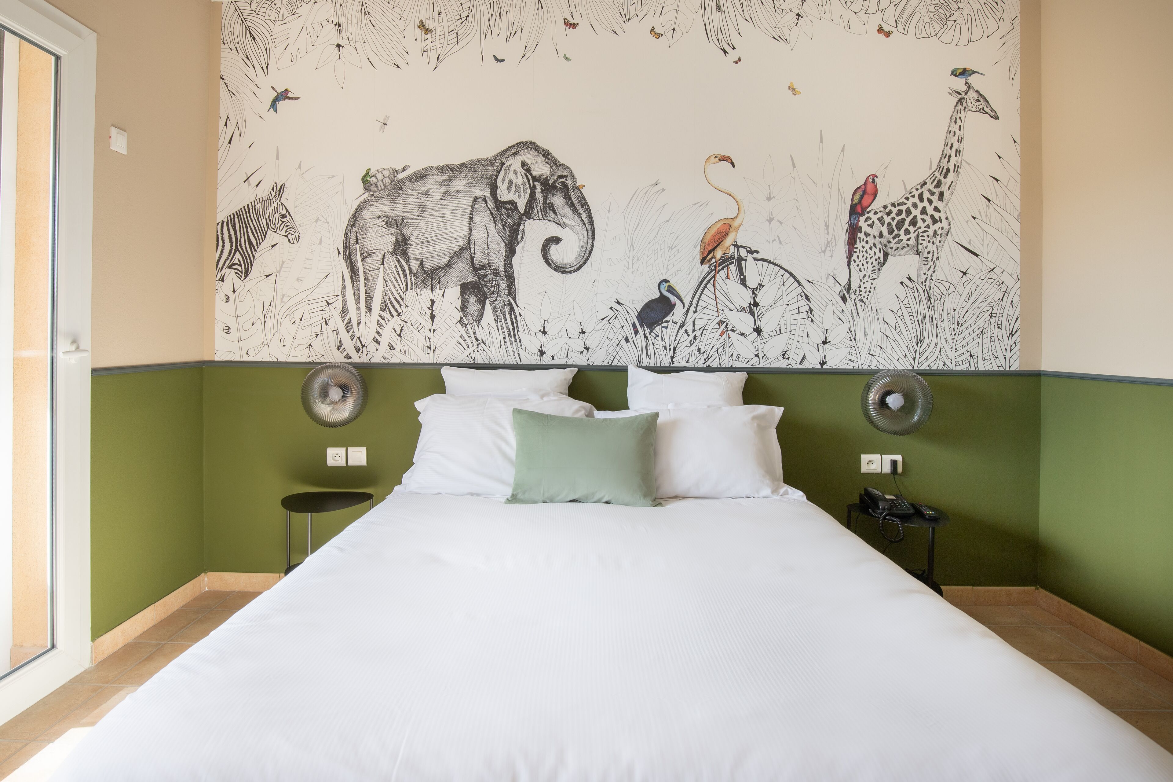 Habitació d'hotel amb un mural gran de fauna a la paret, un llit amb roba blanca i una paret decorativa de color verd.
