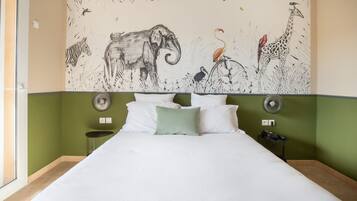 Habitació d'hotel amb un mural gran de fauna a la paret, un llit amb roba blanca i una paret decorativa de color verd.