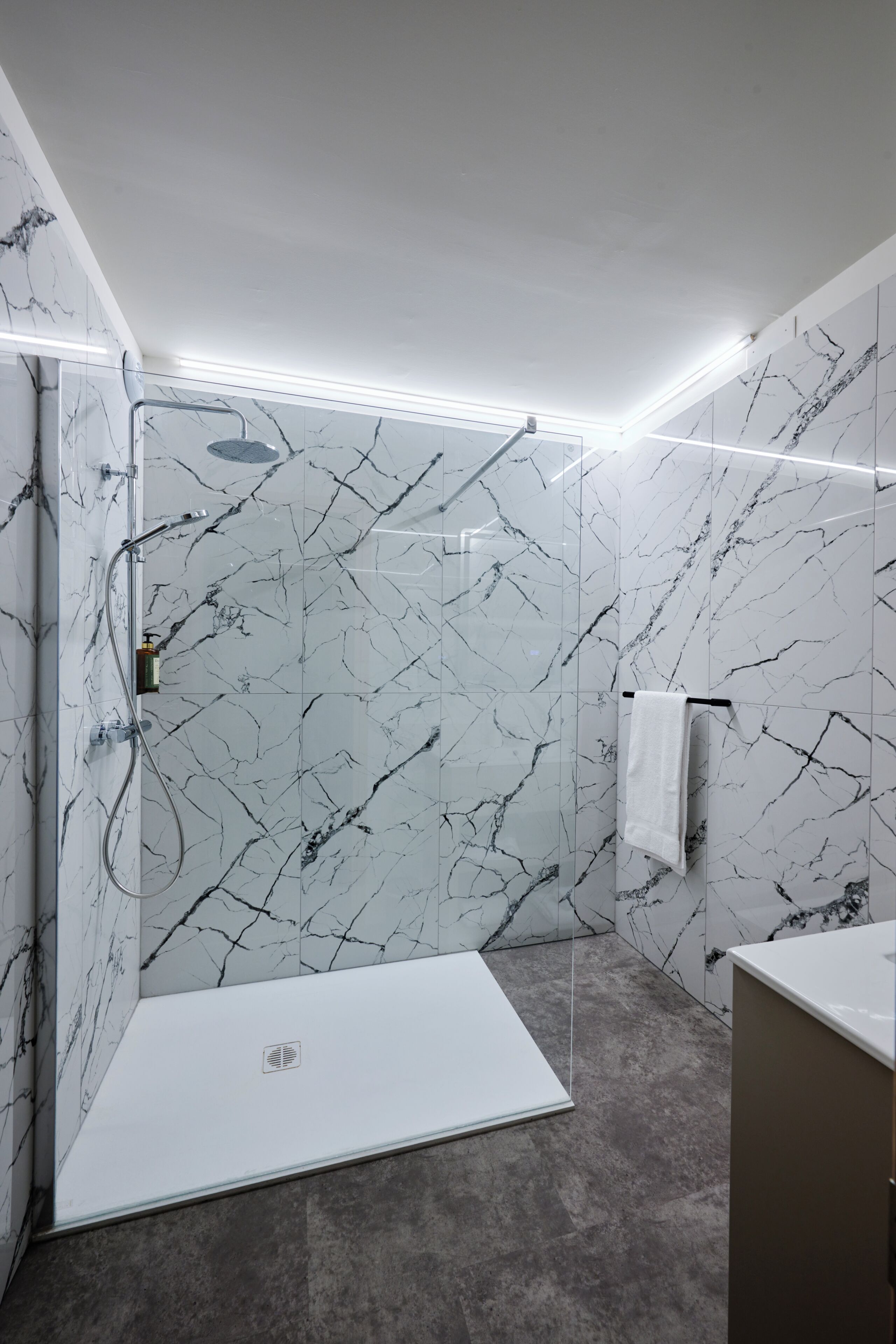 Un baño moderno con paredes de mármol, zona de ducha y tocador.