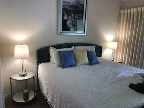 A neatly made bed with a white bedspread and multiple pillows in blue and beige. There are two bedside lamps on either side of the bed, and a framed picture above it. - 2 D, Three Bedroom Townhome (Miramar Beach)