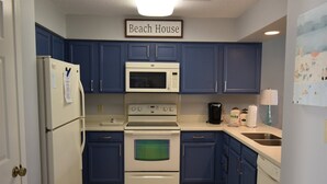 A kitchen with blue cabinets, a white refrigerator, a microwave, an oven, and a coffee maker. - 2 D, Three Bedroom Townhome (Miramar Beach)