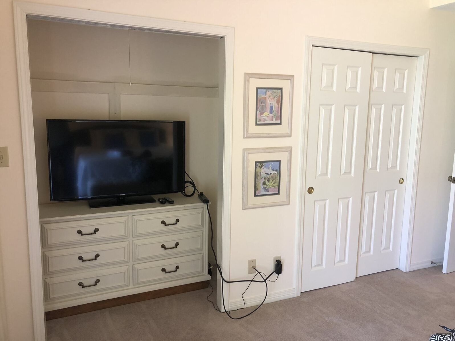 A room with a TV on a white cabinet, a door, and two framed pictures on the wall.