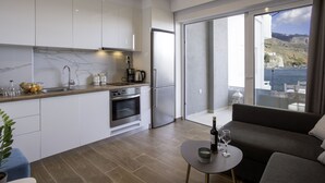 Een moderne keuken met witte kastjes, een marmeren spatwand en roestvrijstalen apparatuur. Er is een balkon met uitzicht op zee en heuvels.