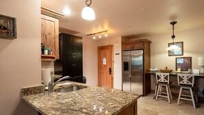 A kitchen with granite countertops, stainless steel appliances, wooden cabinets, and a bar area with stools. - Jupiter Inn (Park City)
