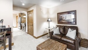 A living room with a brown leather sofa, a woven ottoman, a table lamp, and a framed picture on the wall. - Jupiter Inn (Park City)