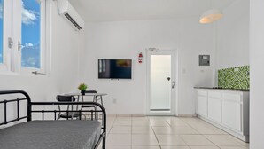 A compact room with a bed, a small table with a chair, a TV, a kitchenette, and a door leading to another room. - Puerto Rico 1 Bed Beach Rental Otium Rentals (San Juan)
