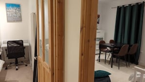 A room with a dining table, chairs, a black office chair, a white radiator, and a green curtain. - Fully-equipped Flat in the City of London (London)