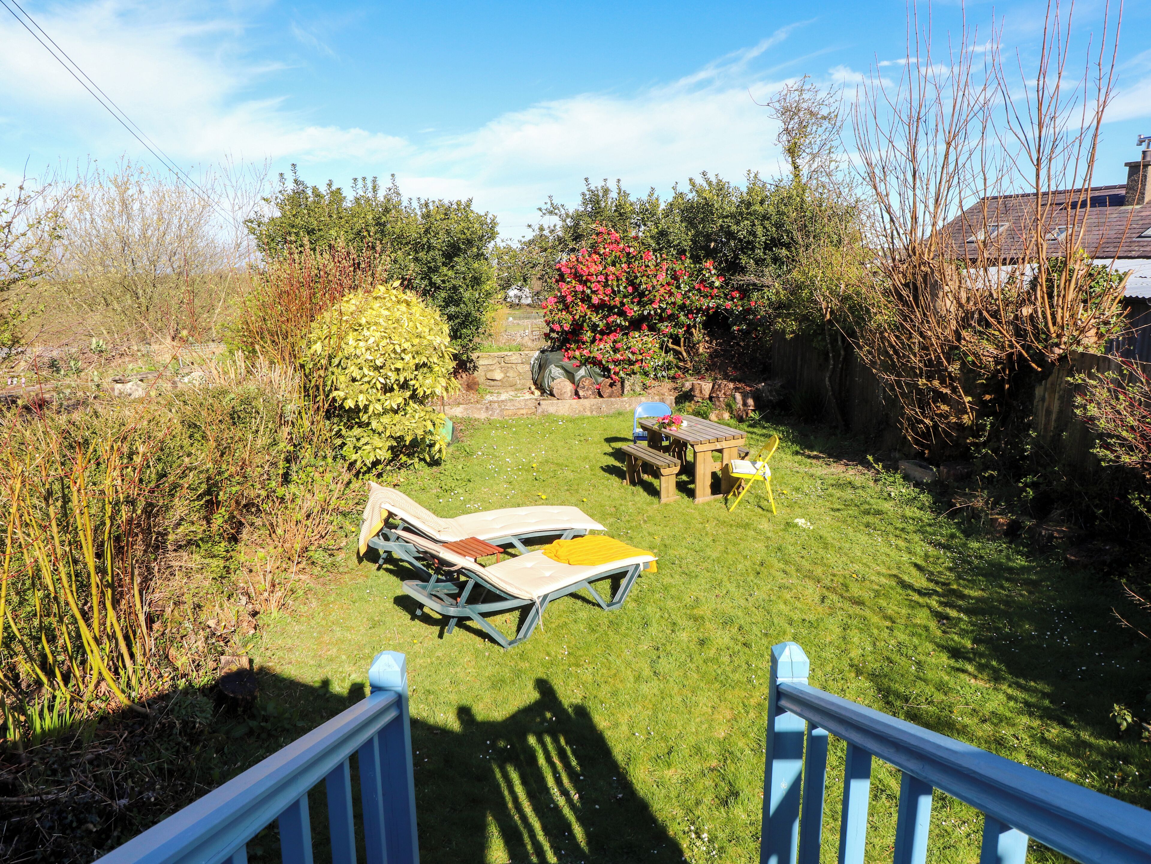 A garden with a wooden table and chairs, a sun lounger, and a small pond.
