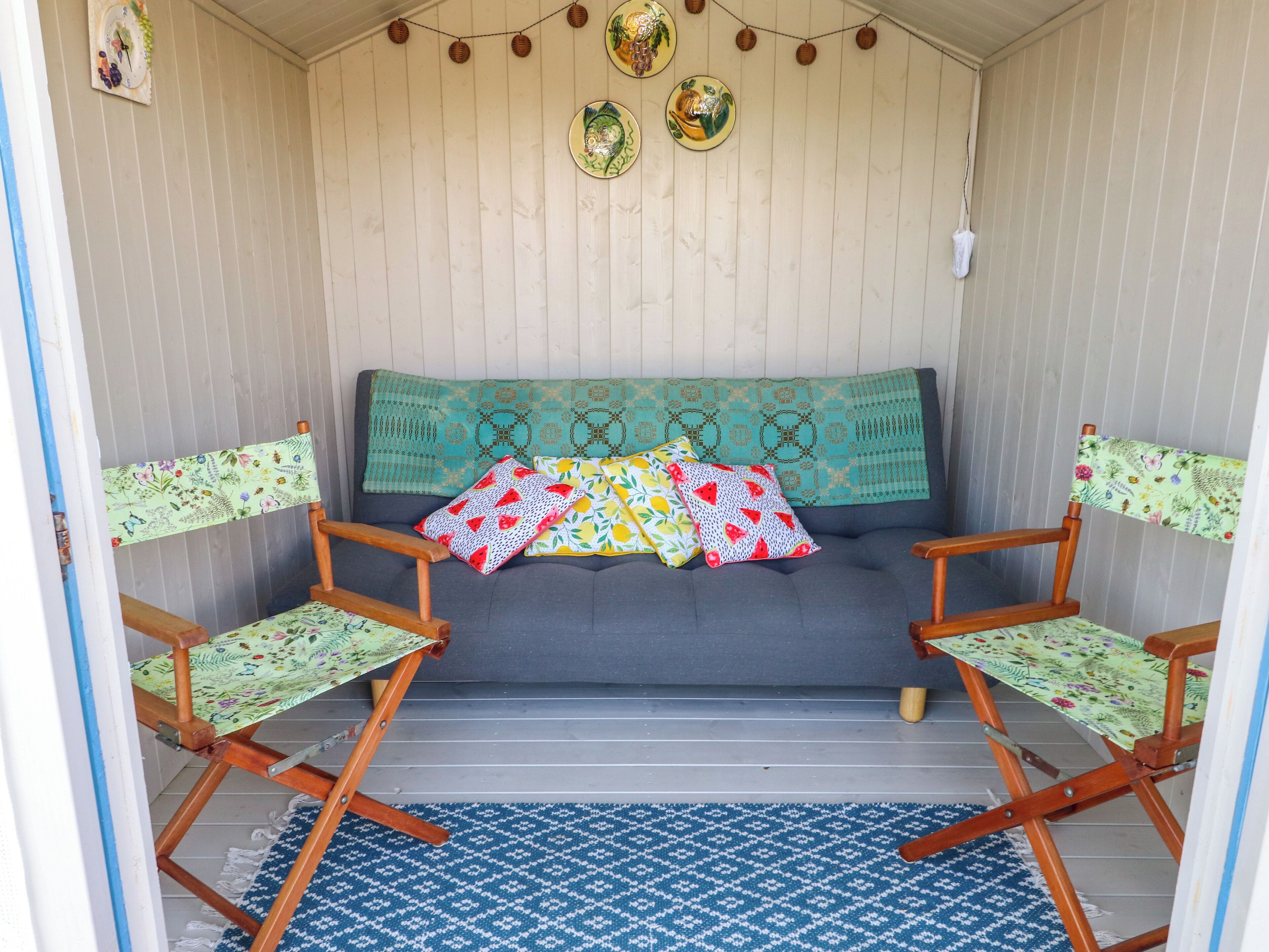 Una habitación acogedora con un sofá, dos sillas de madera, un tapete estampado y adornos en las paredes.