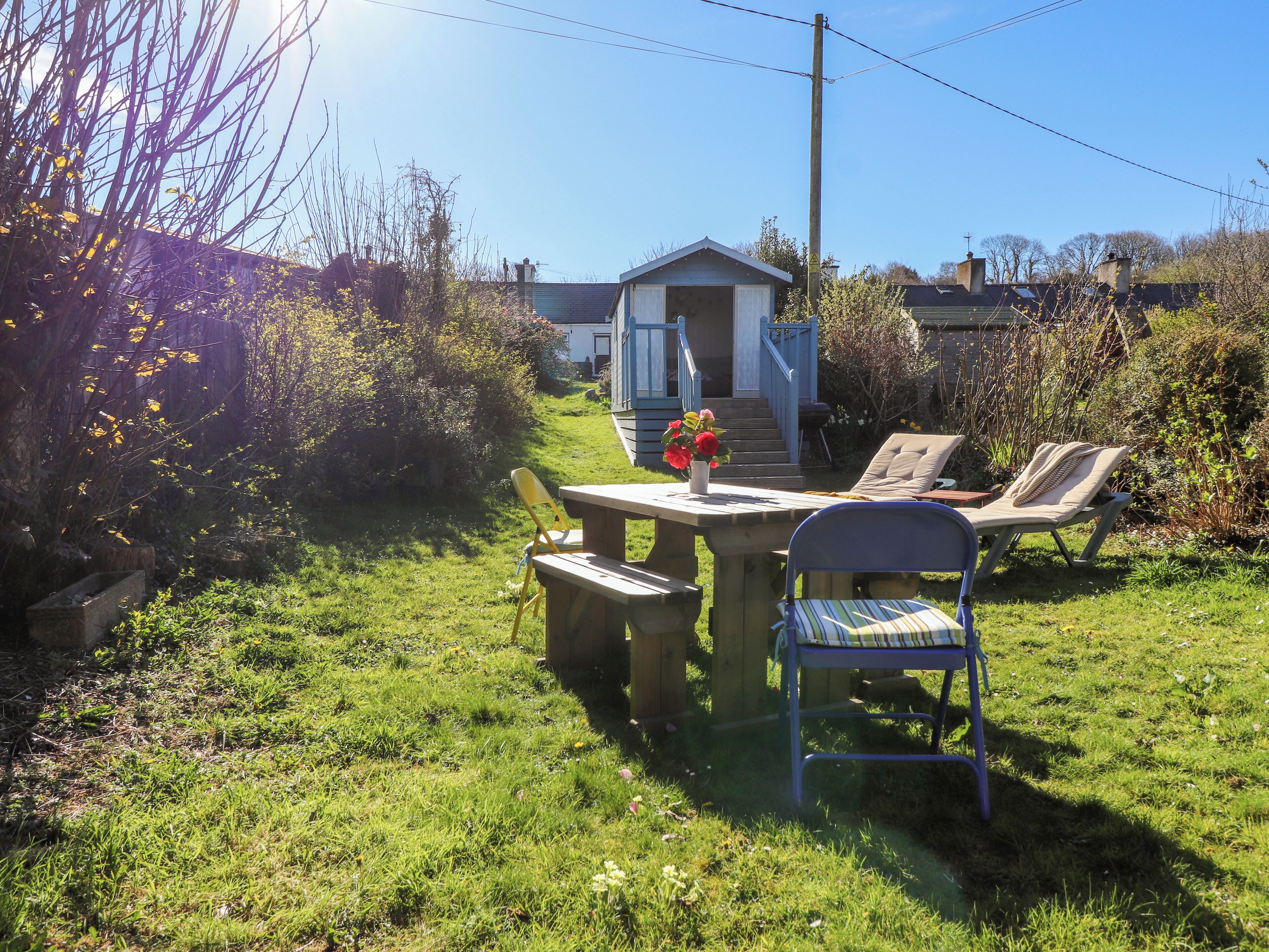 A garden with a wooden table, two chairs, and a small shed in the background.