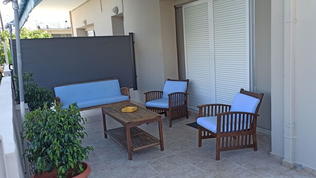 Eine Terrasse mit einer Couch, zwei Stühlen, einem Tisch und einem Blumentopf.