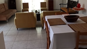 Ein geräumiges Wohnzimmer mit Essbereich, ausgestattet mit einer Couch, Sesseln, einem für das Essen gedeckten Tisch und einer Deckenleuchte.