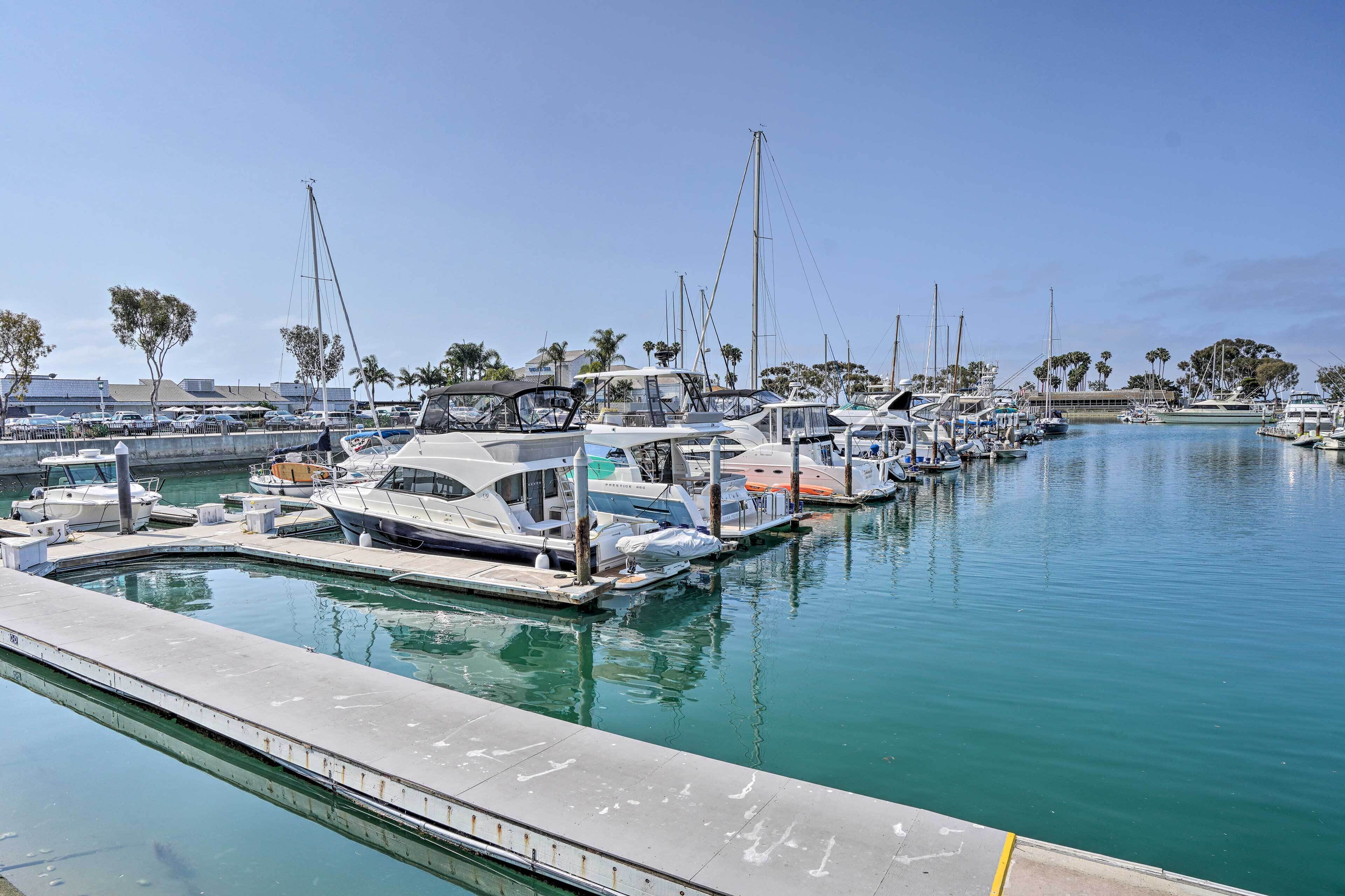 Un port de plaisance où sont amarrés de nombreux bateaux, un ciel dégagé et des palmiers en arrière-plan.