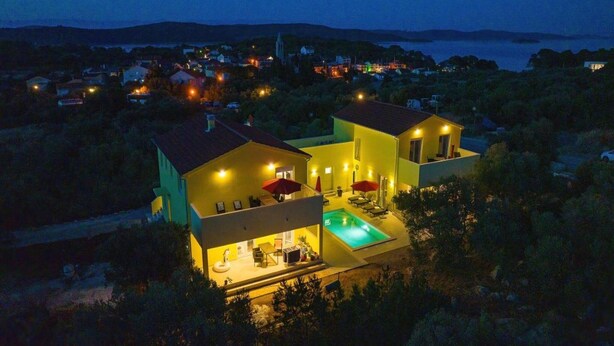 A modern two-story house with a swimming pool, surrounded by greenery and a view of a town at dusk. - Luxury Villa Gaby With Heated Pool (Sali)