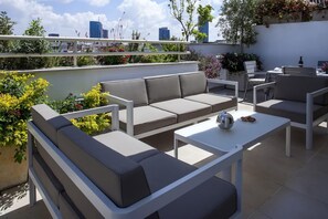 A rooftop terrace with a grey sofa, white armchairs, and a white coffee table. There are potted plants and flowers around the seating area. - Melchett Plume in Tel Aviv-yafo (Tel Aviv)