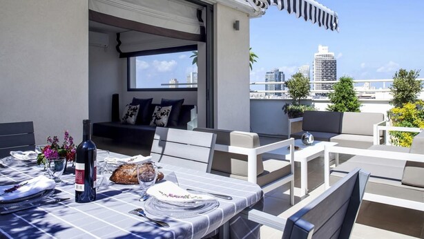 A rooftop terrace with a dining table set for two, a sofa, and a view of the city skyline. - Melchett Plume in Tel Aviv-yafo (Tel Aviv)