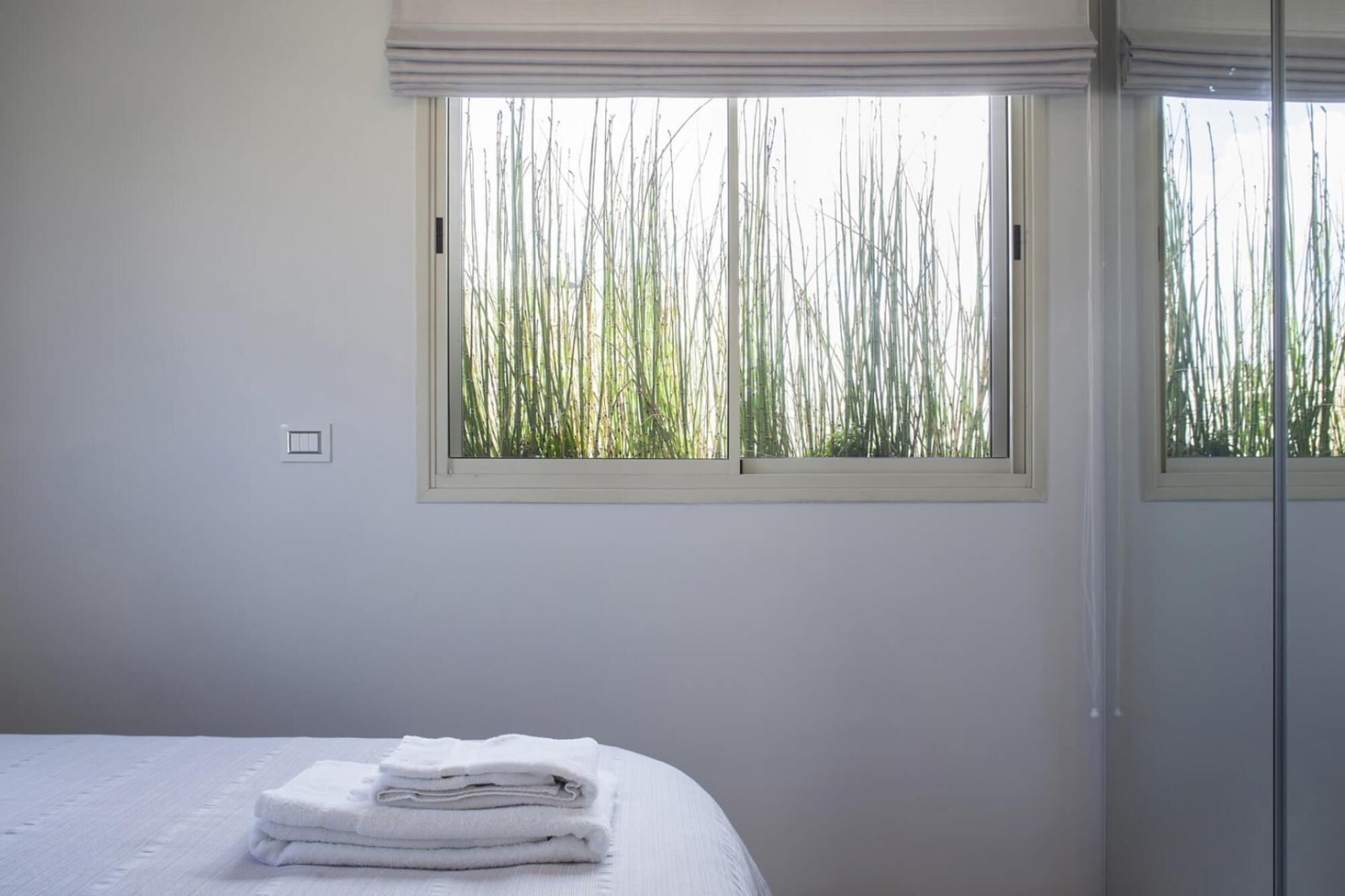 A bedroom with a bed, a window with a view of tall grass, and a door.