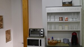 A compact kitchen with a microwave, toaster, and refrigerator. A shelf above the refrigerator holds glassware and a basket.