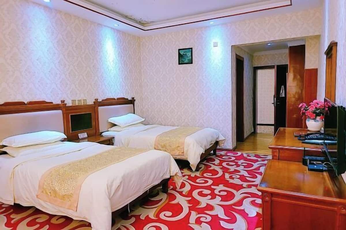 A hotel room with two beds, a wooden desk, a TV, and a red patterned carpet.