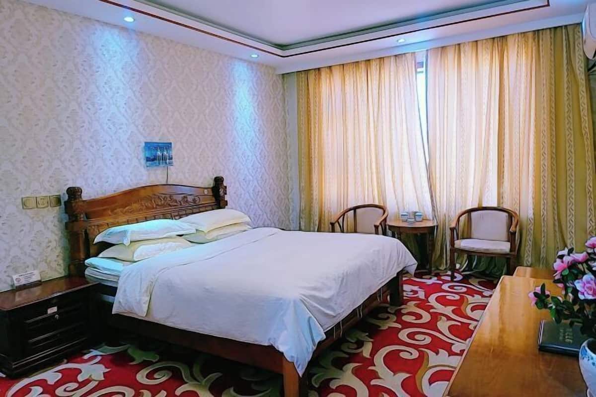 A hotel room with a bed, two chairs, a small table, and a vase with flowers.
