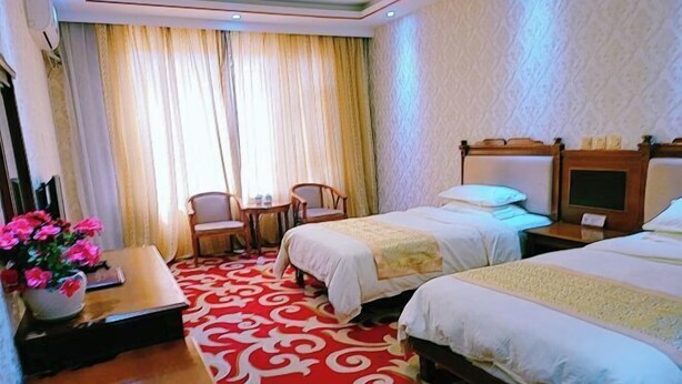 Une chambre d’hôtel avec deux lits, un bureau avec une chaise, une petite table et une grande fenêtre avec des rideaux.