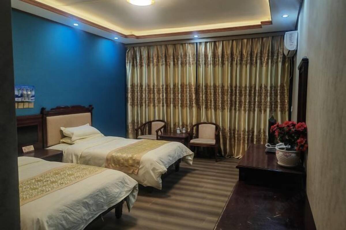 A hotel room with two beds, a desk, a chair, and a potted plant.