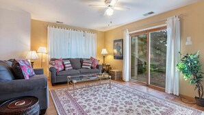 A living room with a sofa, two lamps, a coffee table, a rug, a ceiling fan, and a sliding glass door leading to a garden. - Amazing Bayview: Swimming Pool, Harbor Views, Downtown Saugatuck, Balcony (Saugatuck)