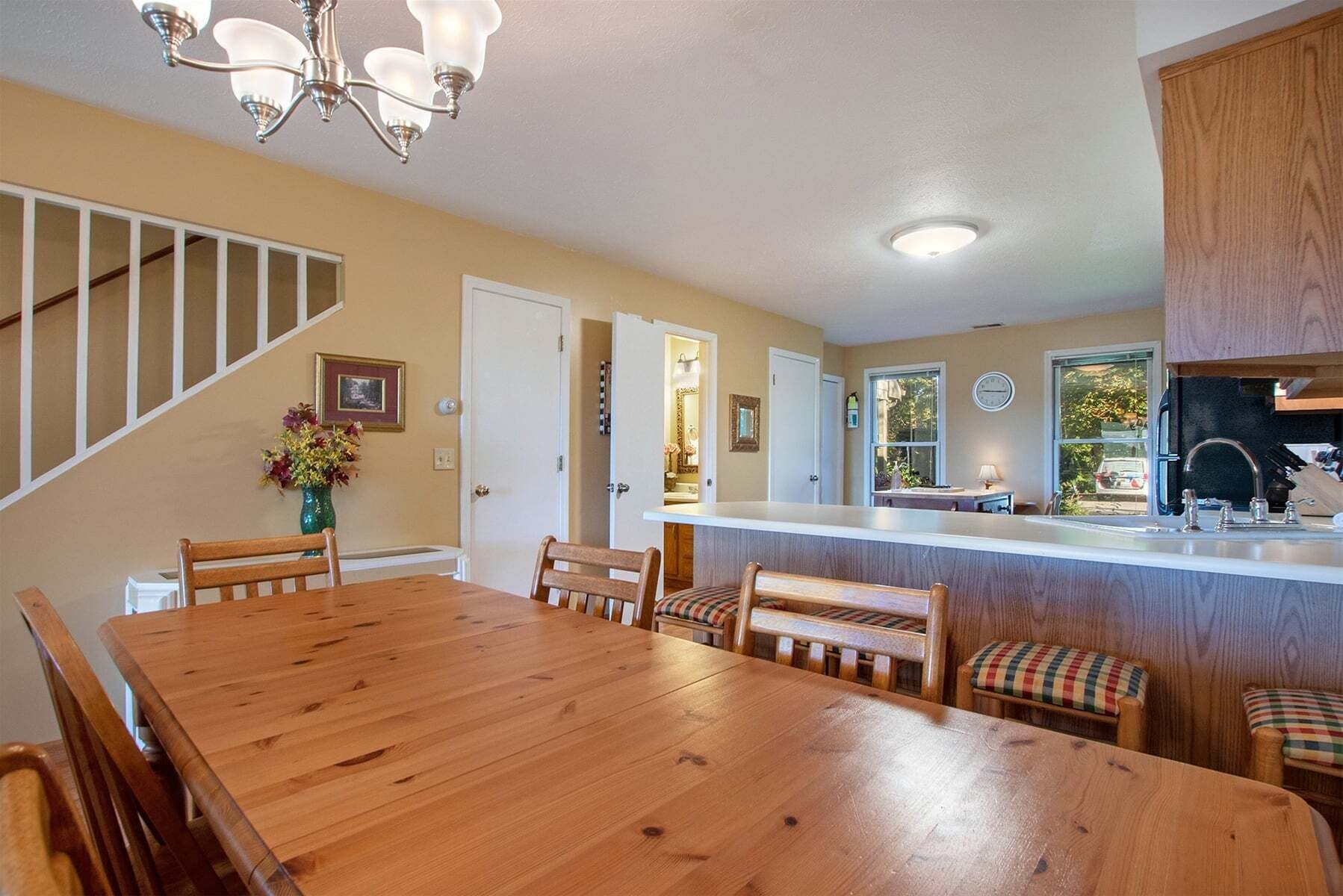 A dining area with a wooden table and chairs, a kitchen with a sink and cabinets, and a staircase with a railing.