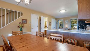 A dining area with a wooden table and chairs, a kitchen with a sink and cabinets, and a staircase with a railing. - Amazing Bayview: Swimming Pool, Harbor Views, Downtown Saugatuck, Balcony (Saugatuck)