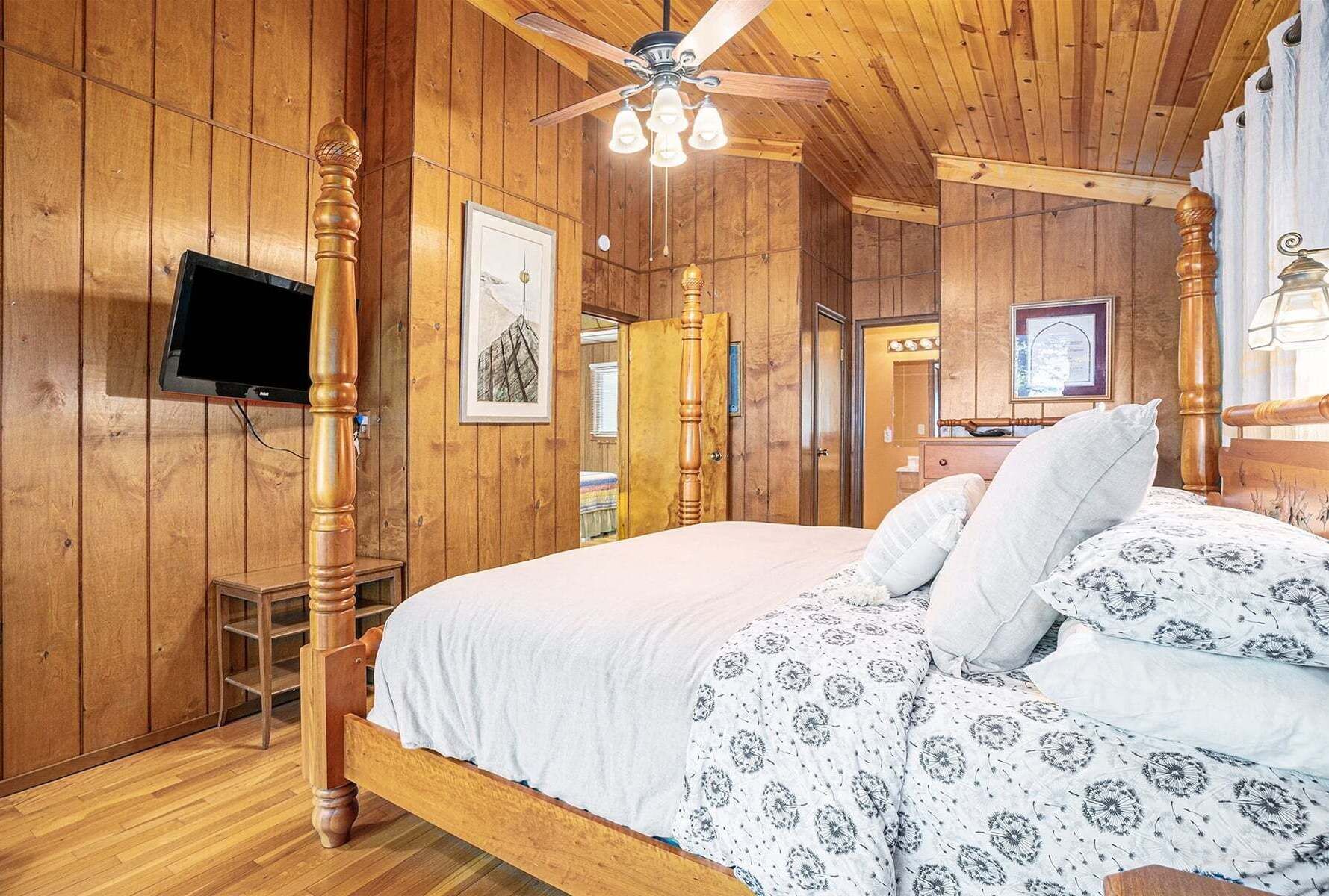Ein Zimmer mit Holzwänden, einem Bett, einem Fernseher und einem Deckenventilator.