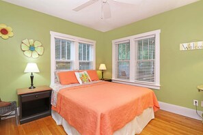 A bedroom with a bed, two nightstands, a chair, and two windows with blinds.