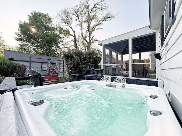 A hot tub in a backyard with a covered patio and a house in the background.