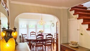 A dining area with a wooden table and chairs, a chandelier, and a staircase with red steps.