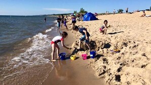 A beach scene with people playing in the sand, a tent, and a clear sky.