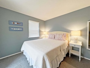 Un dormitorio con una cama, dos mesitas de noche, una ventana con persianas y decoración en la pared.