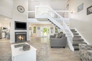 Amplia sala de estar con chimenea, una escalera y una cocina moderna al fondo.