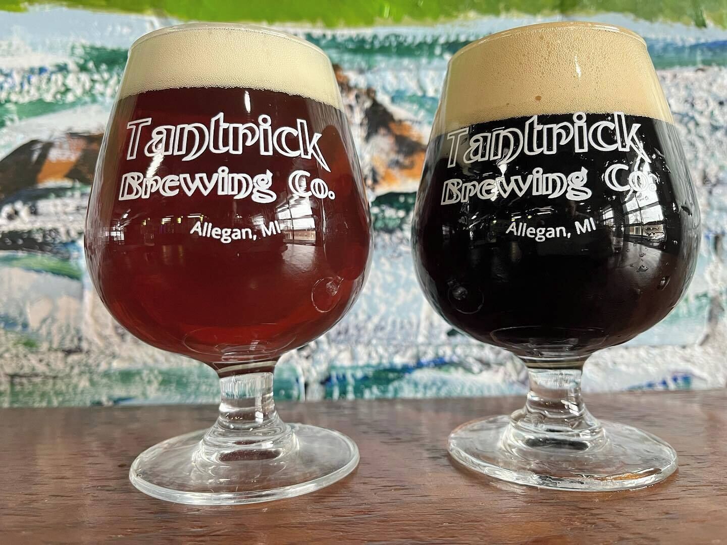 Two glasses of beer with 'Tantrick Brewing Co.' and 'Allegan, MI' on them, placed on a wooden surface.