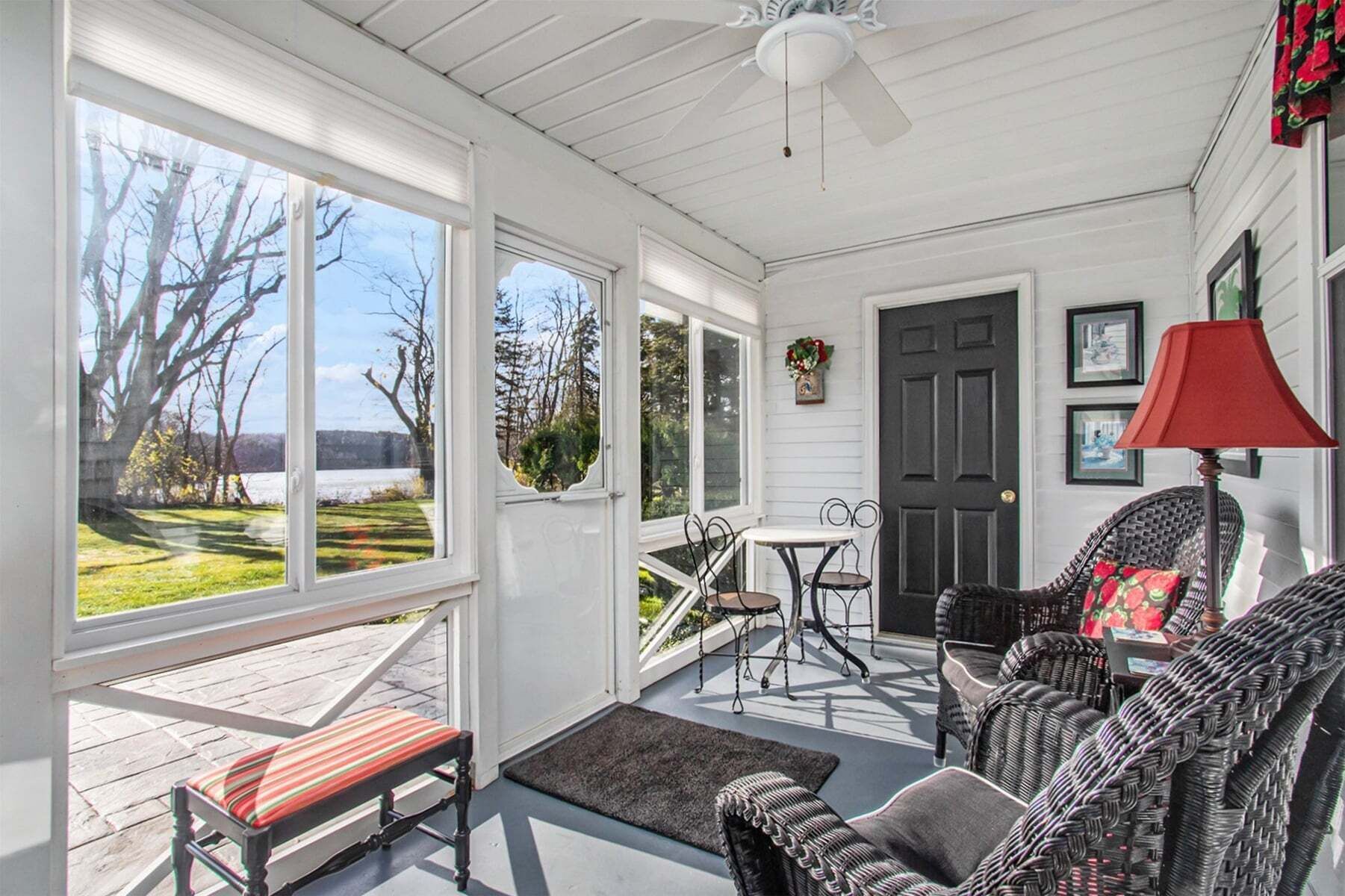 A covered porch with a bench, wicker chairs, a table, and a door.