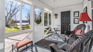 A covered porch with a bench, wicker chairs, a table, and a door. - The Old Snow Farm: Lake Allegan Waterfront, Classic Farmhouse, Fire Pit, Patio (Allegan)