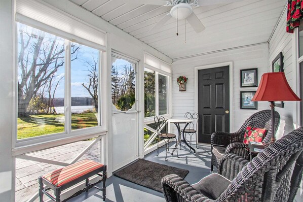 A covered porch with a bench, wicker chairs, a table, and a door.