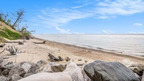 Ein Strand mit großen Felsen, blauem Himmel und ruhigem Wasser.