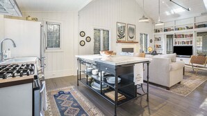 A kitchen with a gas stove, a sink, and a dining area with a table and chairs. There are bookshelves and a television in the living area.