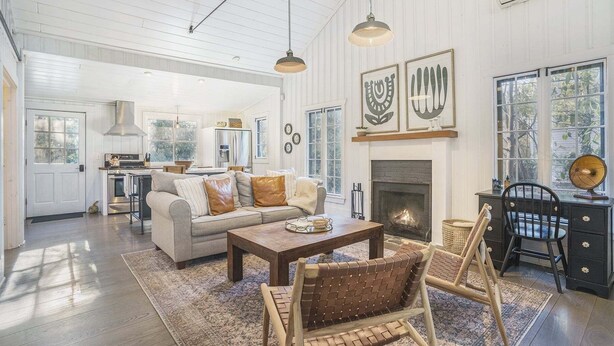 A spacious living room with a fireplace, a dining area, and a kitchen in the background.