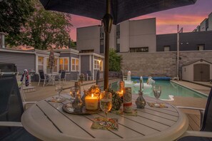 A poolside table set with drinks and candles, surrounded by chairs and a pool with inflatable unicorns. - Saugatuck Lodge: Private Pool, Hot Tub, Fireplace, Downtown Saugatuck, Sleeps 22 (Saugatuck)