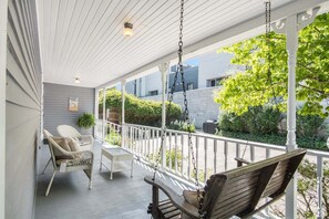 A covered porch with wicker chairs, a swing, and a small table.