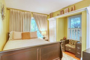 A bedroom with a bed, curtains, a nightstand, a lamp, a dresser, and a window with blinds.