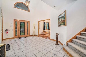 A spacious foyer with a tiled floor, a wooden staircase, a fire extinguisher, and a painting on the wall. - Great Escape: Spacious, Home Theater, Fire Pit, Walk to Downtown (Saugatuck)
